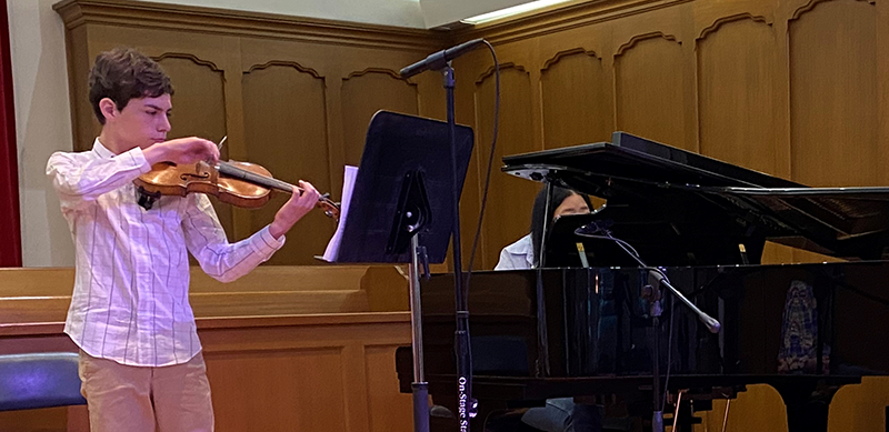 Young man playing violin with woman accompanying on piano
