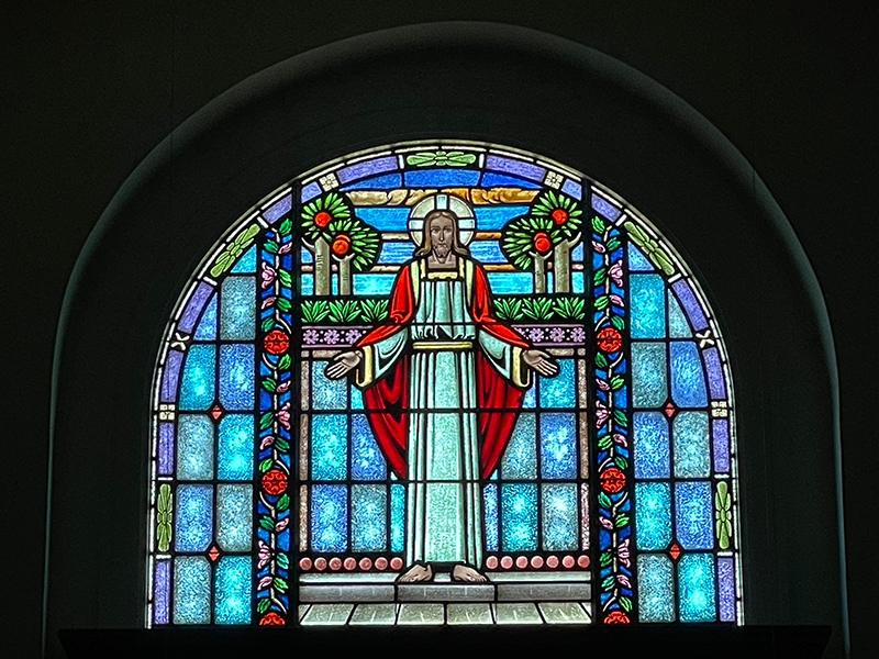 Stained glass window depicting a welcoming image of Jesus